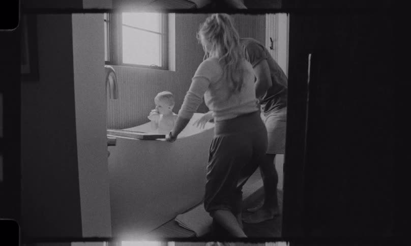A loving mother and father take turns bathing their baby in a modern bathtub in a nostalgic black and white home movie
