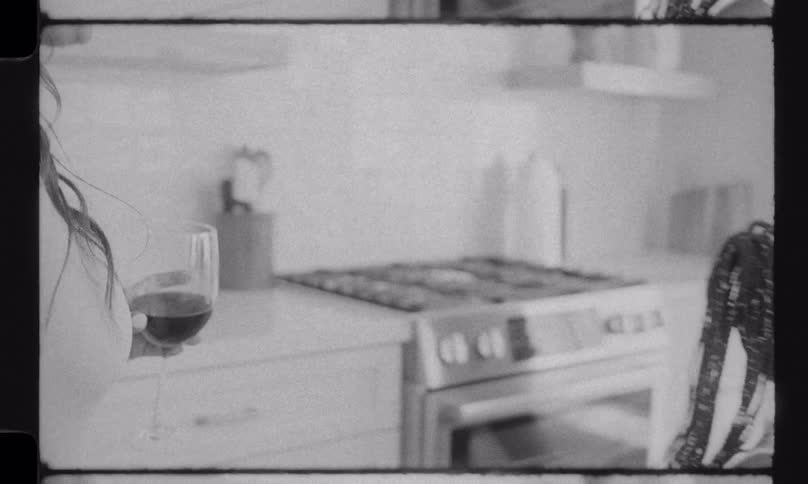 A nostalgic, black and white vintage film captures a mother and daughter preparing a meal in the kitchen while the mother enjoys a glass of wine