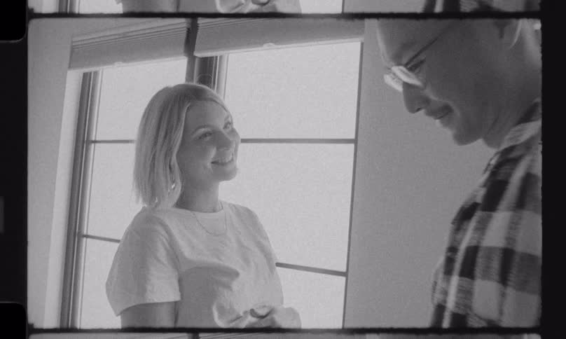 Vintage-style black and white footage captures a happy, expectant couple sharing a tender kiss while preparing clothes for their baby