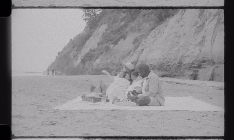 Retro 8mm film captures a happy family enjoying a quiet picnic together on a sandy beach