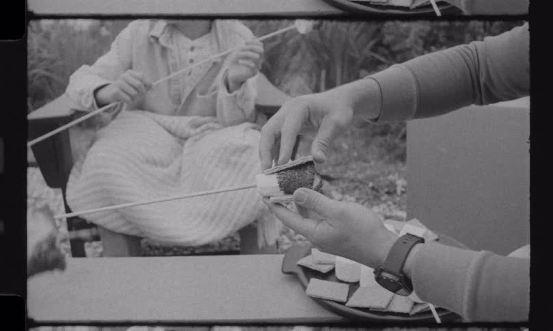 A person slowly assembles a s'more with a toasted marshmallow and chocolate in vintage black and white footage