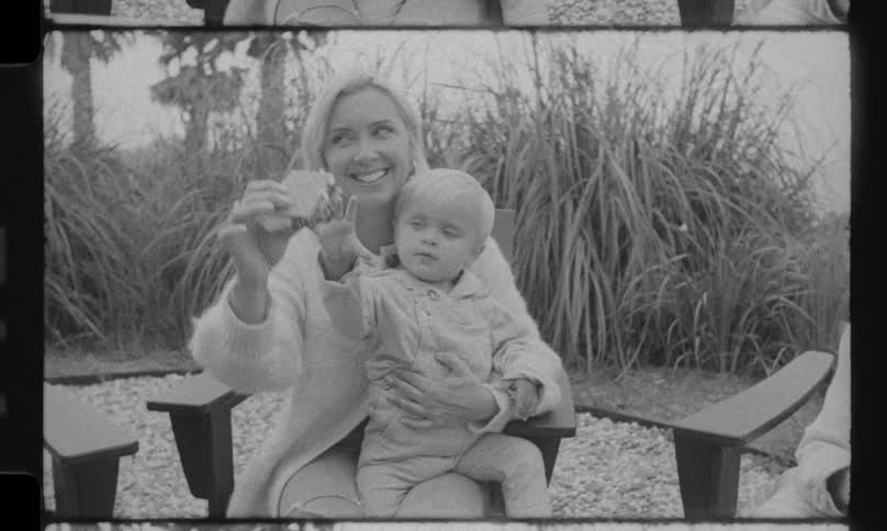 A mother holds her toddler as they are handed a freshly made s'more by the father in this black and white home movie
