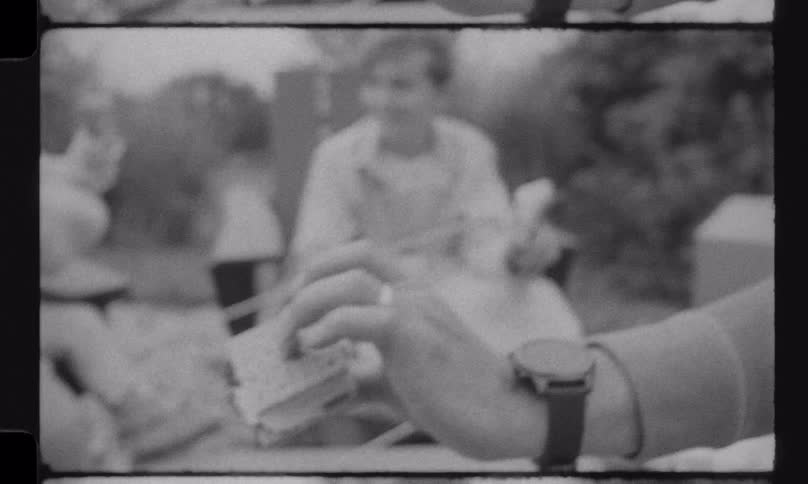 A mother smiles as she helps her young son eat a messy s'more in this charming black and white vintage home movie