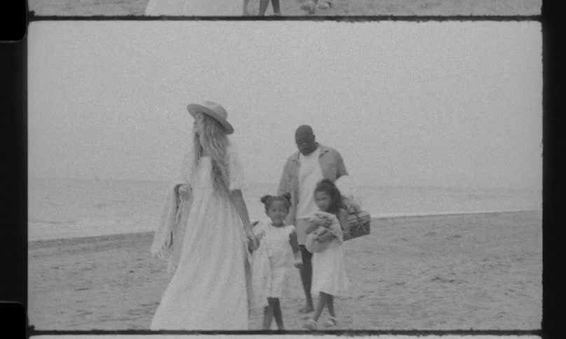 A family with three young daughters walks along the sandy shore for a picnic in this nostalgic, black and white vintage-style footage