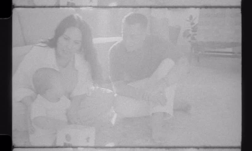Nostalgic black and white home video footage shows a loving young family playing with their baby on the floor