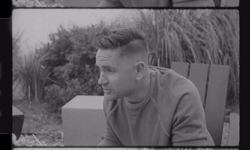 Nostalgic black and white footage shows a family laughing and roasting marshmallows together around an outdoor fire pit
