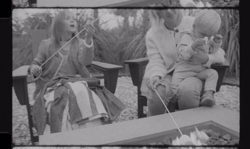 A happy family roasts marshmallows together around a fire pit in this nostalgic black and white, vintage-style home movie