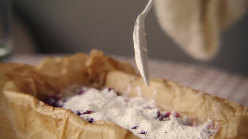 Close up slow motion of a spoon sprinkling flour over fresh berries in a parchment-lined baking dish
