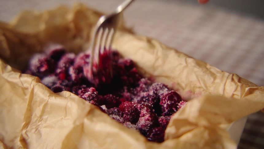 Close-up of a hand gently mixing fresh raspberries and sugar with a fork in a parchment-lined dish