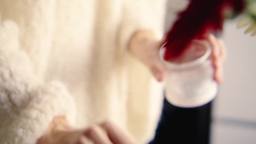 Close up slow motion shot of hands in a cozy sweater scooping moisturizing cream from a small jar