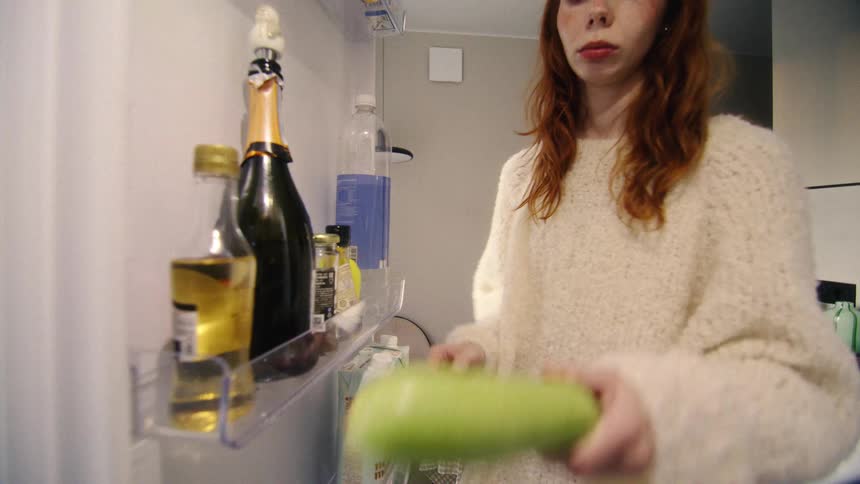A view from inside the refrigerator shows a young woman with red hair opening the door, taking a zucchini, and closing it