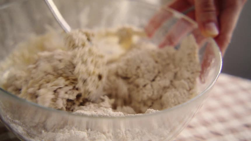 A baker carefully mixes dry and wet ingredients with a fork in a glass bowl in slow motion