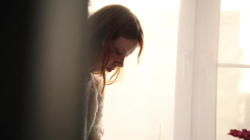 An intimate slow-motion shot reveals a woman in a warm sweater preparing dough by a bright window