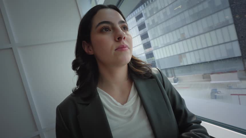 A thoughtful businesswoman pauses from her phone to gaze out the window of her modern office, contemplating the city