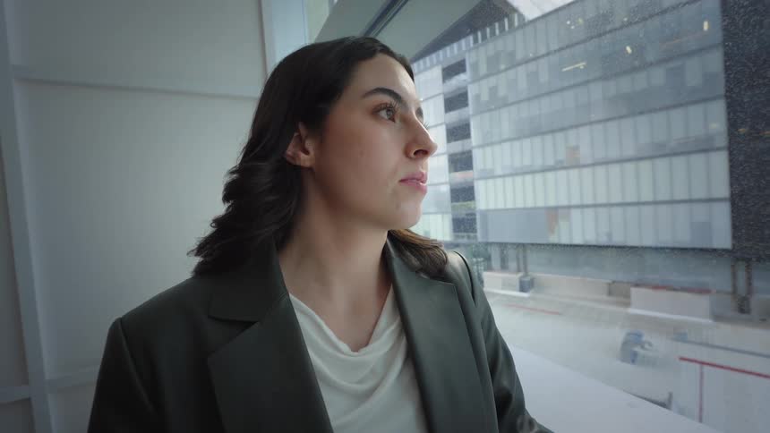 A young businesswoman receives good news on her phone and smiles while looking out her office window at the city