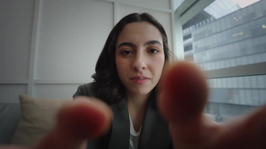 A young woman in a city office looks directly into the camera from a close-up, point-of-view perspective