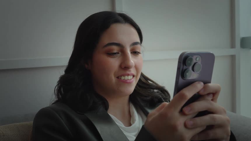 Smiling professional woman texting on her phone while sitting comfortably indoors by a window