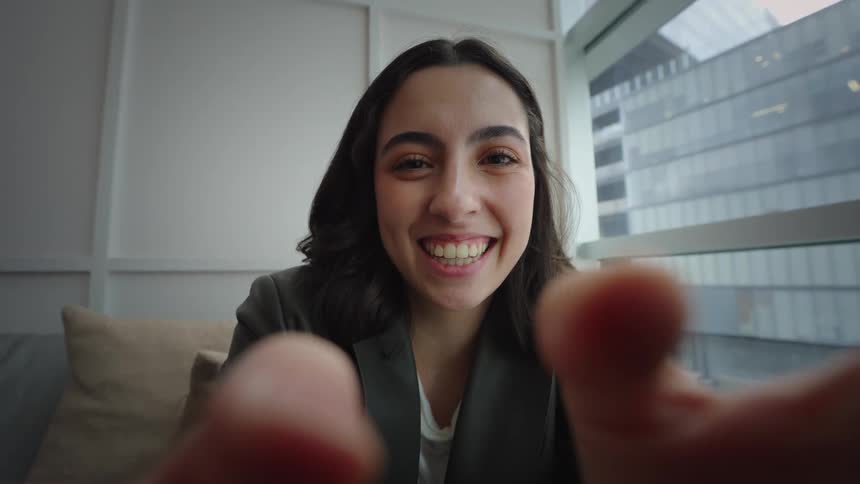 POV of a young woman smiling happily during a video call, with her hands blurred in the foreground as if holding the device