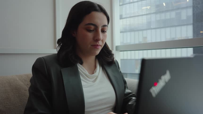 A serious young businesswoman concentrates while working on her laptop in a contemporary office space