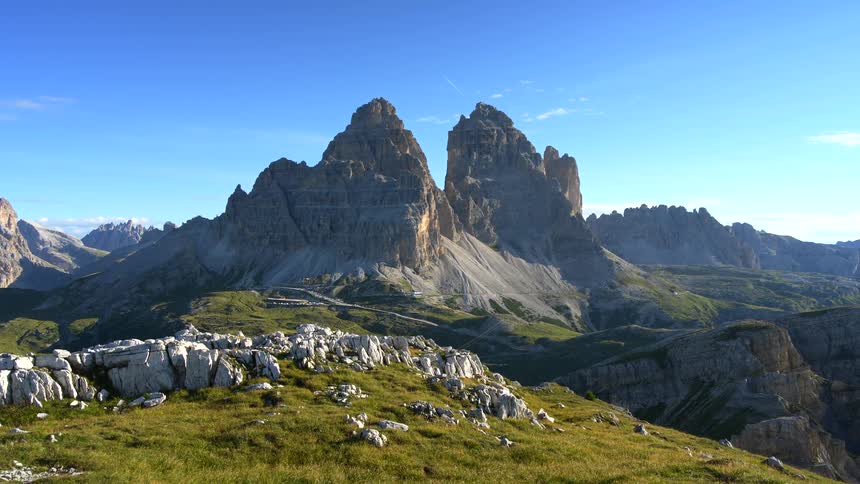 A stunning, static shot of the iconic Tre Cime di Lavaredo mountain peaks in the Italian Dolomites against a clear blue sky