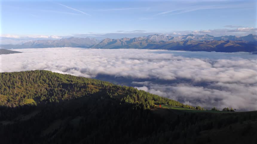 A stunning aerial view captures a sea of clouds filling a valley between lush green mountains under a clear blue sky