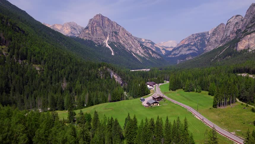 Breathtaking aerial view of a lush green valley with traditional houses nestled between the towering peaks of the Dolomites