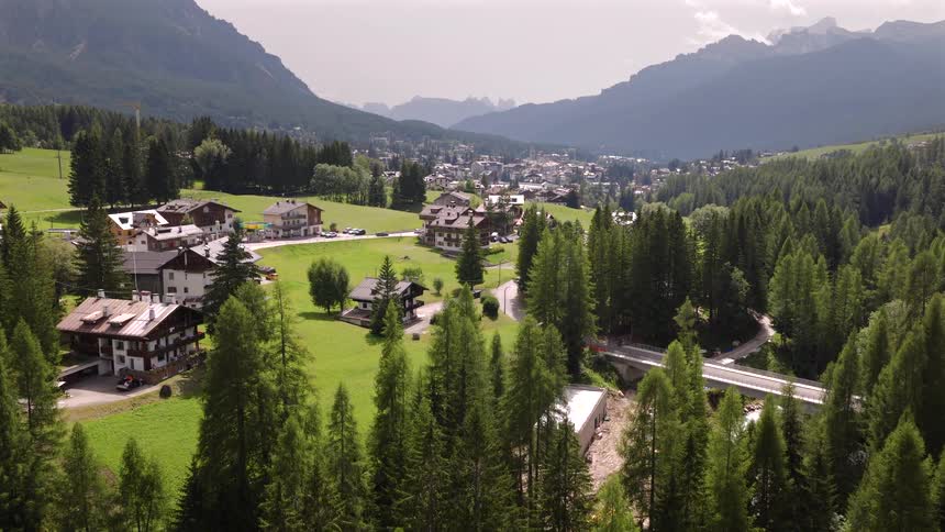 An idyllic aerial view reveals a charming mountain village nestled in a lush green valley surrounded by forests and peaks