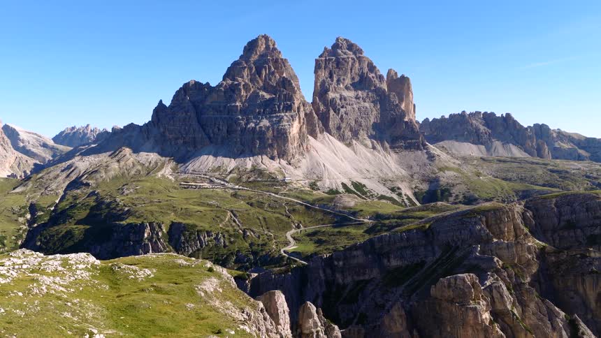 An epic aerial view of the iconic Tre Cime di Lavaredo mountain peaks in the Italian Dolomites against a clear blue sky