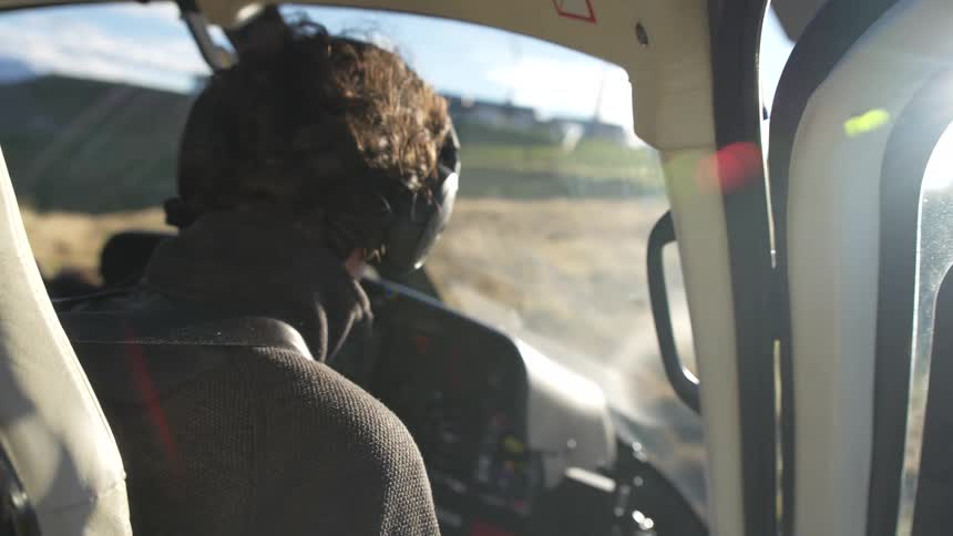Helicopter pilot prepares for takeoff, putting on a headset and checking controls in the sunlit cockpit