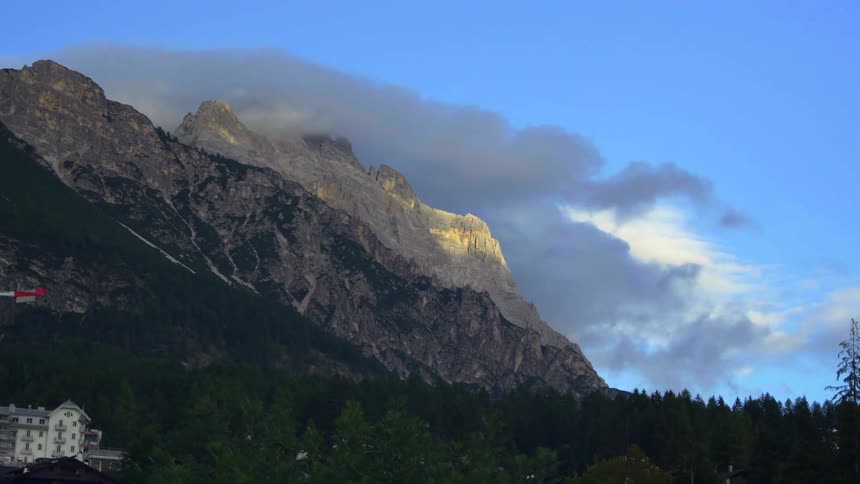 A scenic timelapse captures clouds rolling over a rugged mountain peak as the golden hour sunlight gives way to twilight