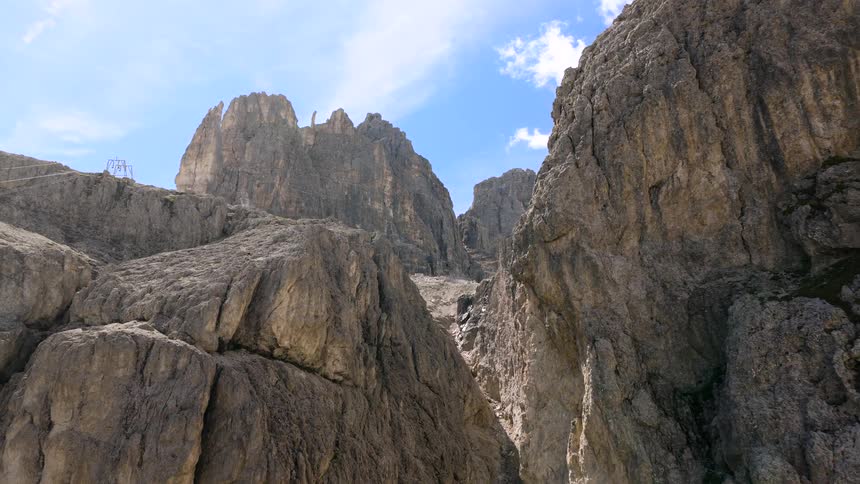 A slow, majestic aerial ascent through a rugged mountain canyon, revealing towering rock formations against a blue sky