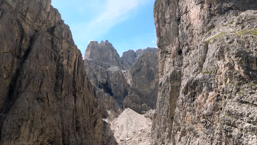 An awe-inspiring aerial view slowly flies through a deep and rugged mountain pass in the Dolomites on a bright, sunny day