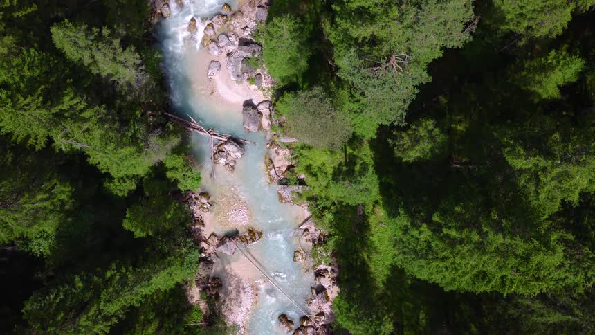An aerial top-down view of a pristine turquoise river flowing through a dense, vibrant green forest