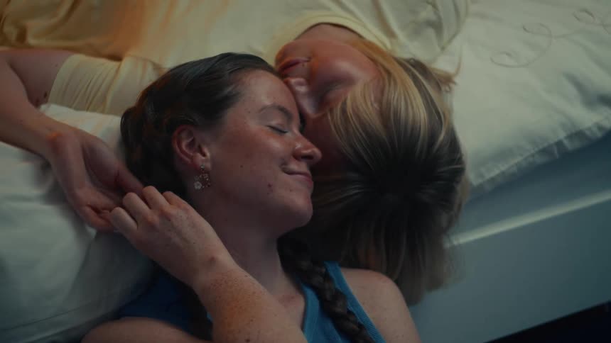 An overhead shot of a loving lesbian couple cuddling affectionately in bed with their eyes closed