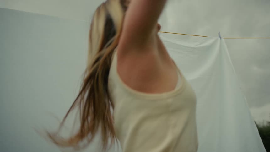 Low angle slow motion shot of a blonde woman dancing expressively with a white sheet behind her