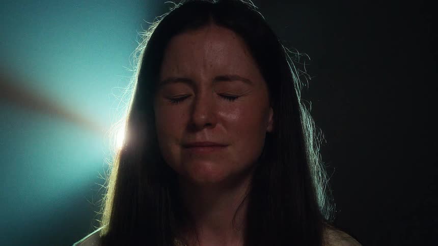 Close up portrait of a woman who closes her eyes and finds a moment of peace and serenity under a spotlight