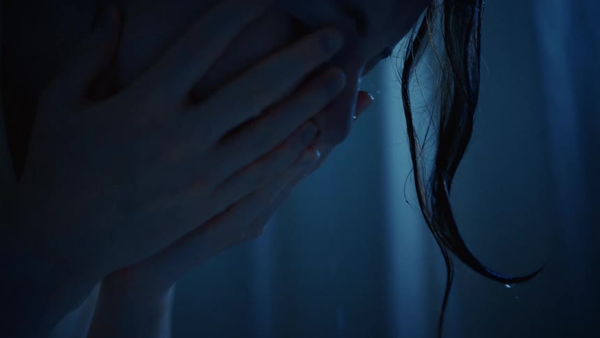 A heartbroken woman with wet hair covers her face and cries in slow motion in a dark, blue-lit setting