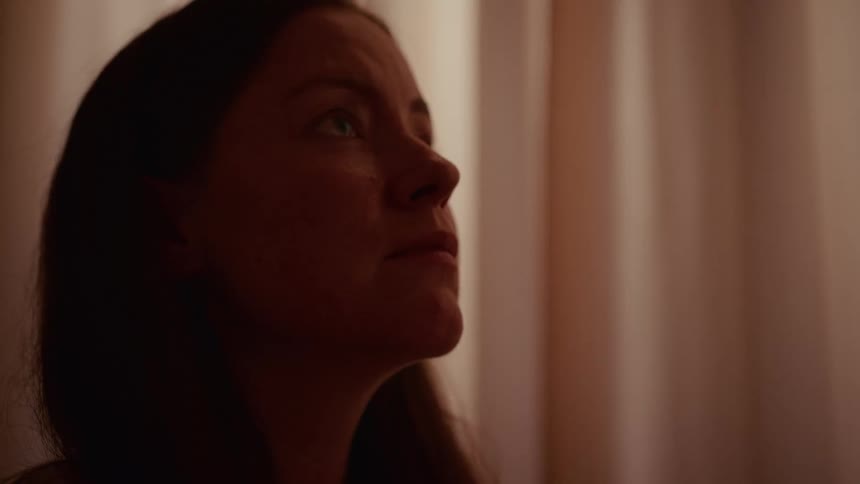 A slow focus pull reveals a close-up of a woman's face as she looks up with a contemplative expression