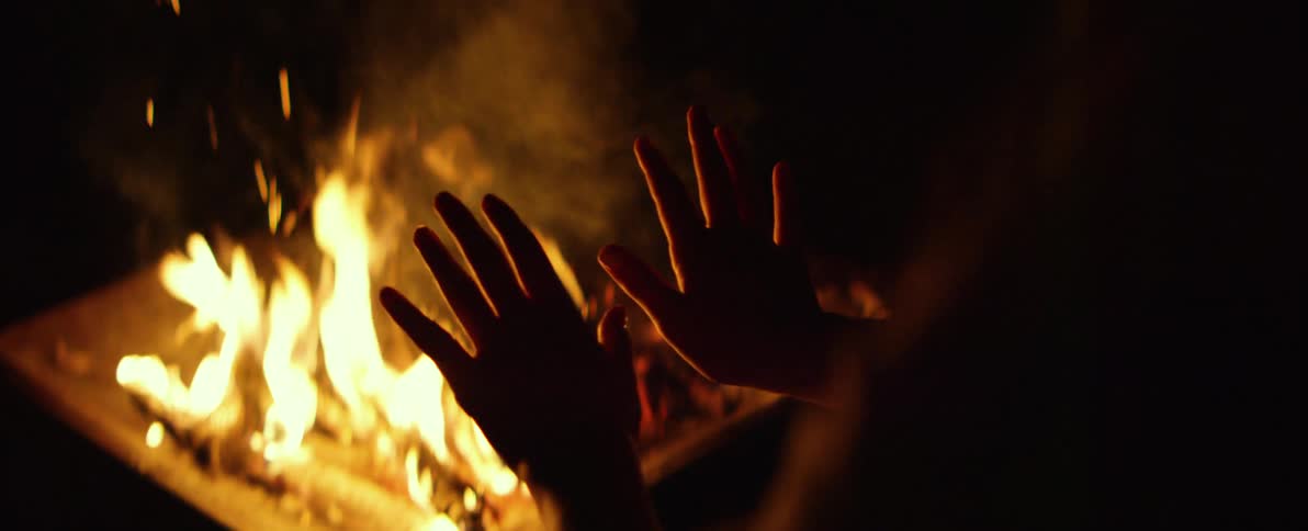 A person's silhouetted hands warming up in front of a cozy bonfire at night