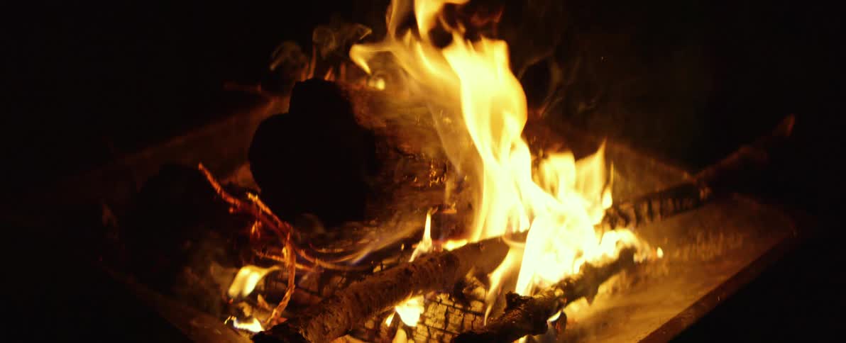 A close-up shot of a roaring campfire burning in a fire pit at night in slow motion