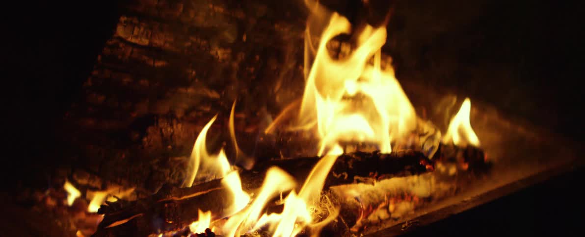 A slow-motion close-up of a warm and cozy fire as the flames dance and the embers glow, slowly coming into focus
