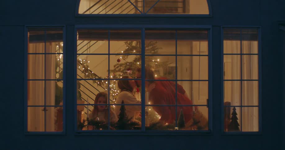 View through a window of a loving family celebrating together at Christmastime in their cozy home at night