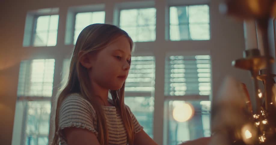 A young girl thoughtfully arranges a wooden king figurine from a nativity set in a cozy, sunlit room