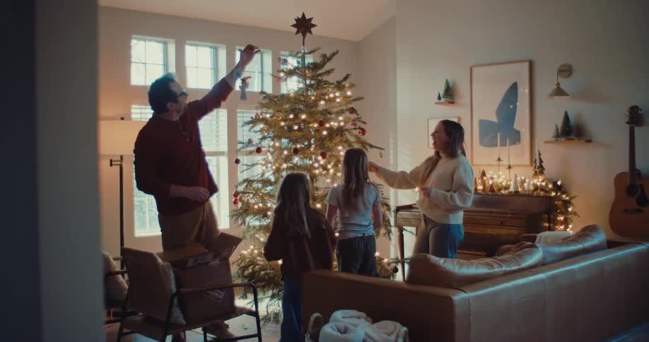 A happy family with two young daughters decorates their Christmas tree together in their cozy living room in slow motion