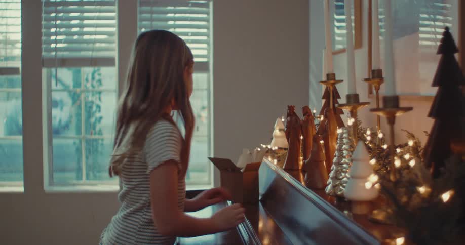 A sweet little girl carefully arranges a wooden nativity scene on top of a piano as she decorates for Christmas