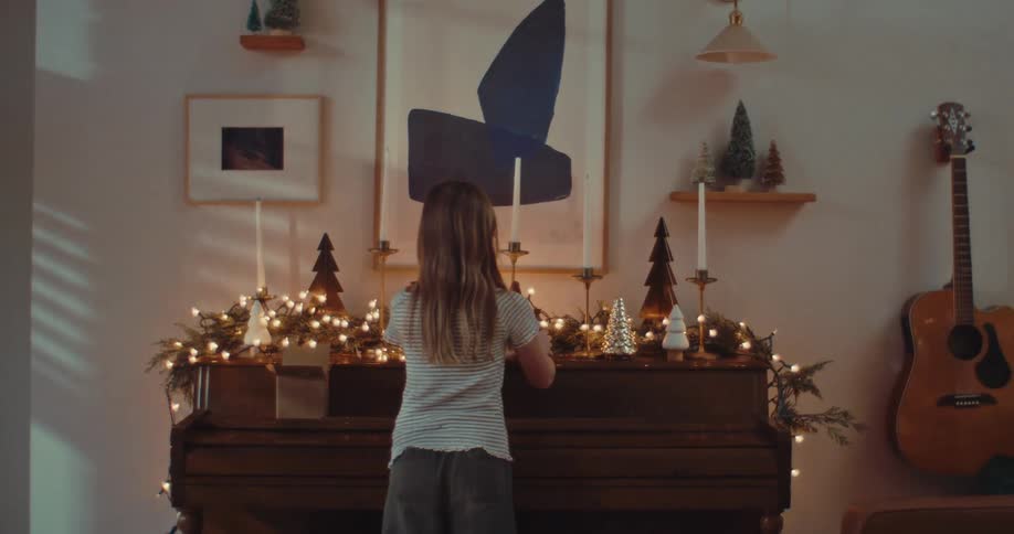 A young girl with her back to the camera sets up a nativity scene on top of a piano decorated for Christmas