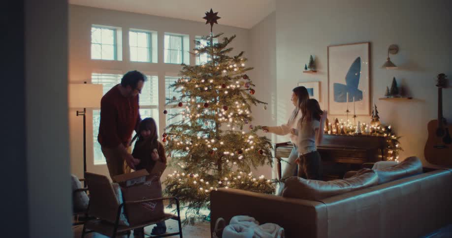 A happy family of four joyfully decorates their Christmas tree together in their cozy living room
