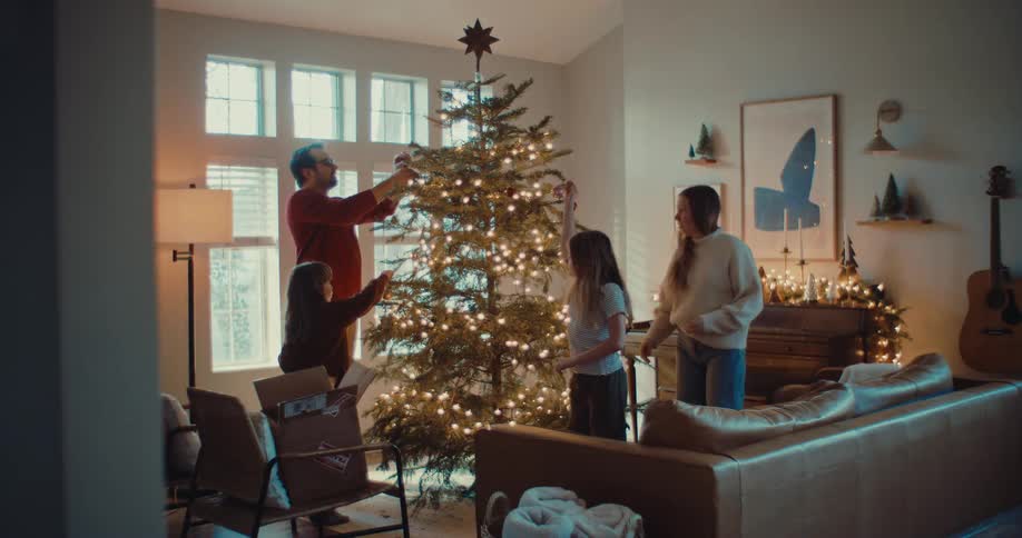 A happy family of four decorates their beautiful Christmas tree together in their cozy living room