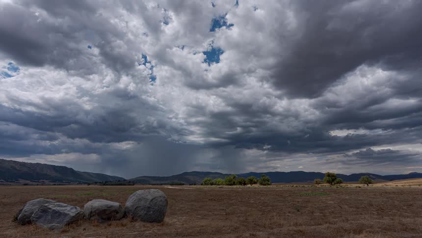 A dramatic time-lapse of dark storm clouds gathering and raining over a wide, arid valley
