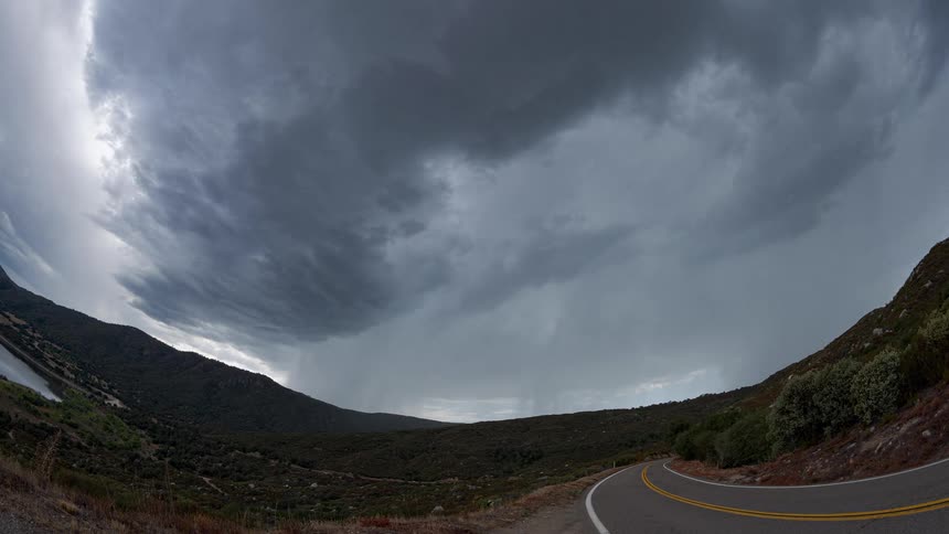 Dramatic wide-angle timelapse of a menacing storm front moving over a rural mountain landscape with a road and lake in view